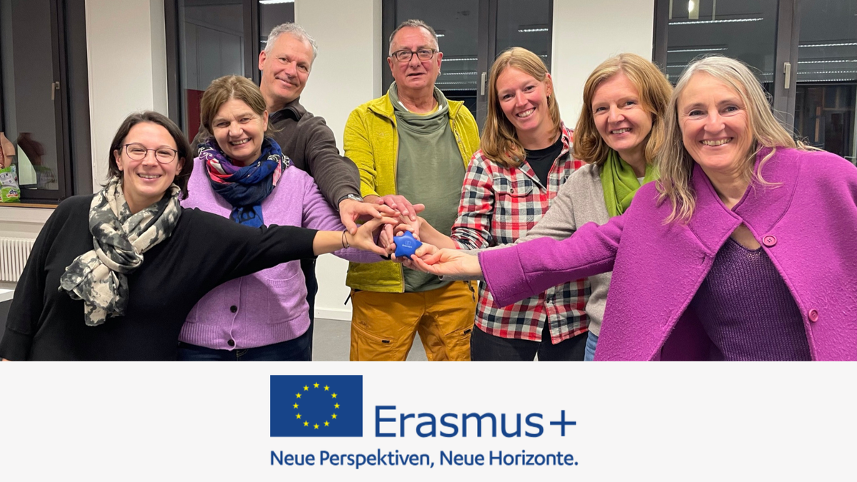 Eine Gruppe von sechs Personen steht in einem Raum und hält gemeinsam einen blauen Stern mit dem Erasmus+-Logo. Erasmus+Logo darunter und die Aufschrift "Neue Perspektiven, Neue Horizonte".