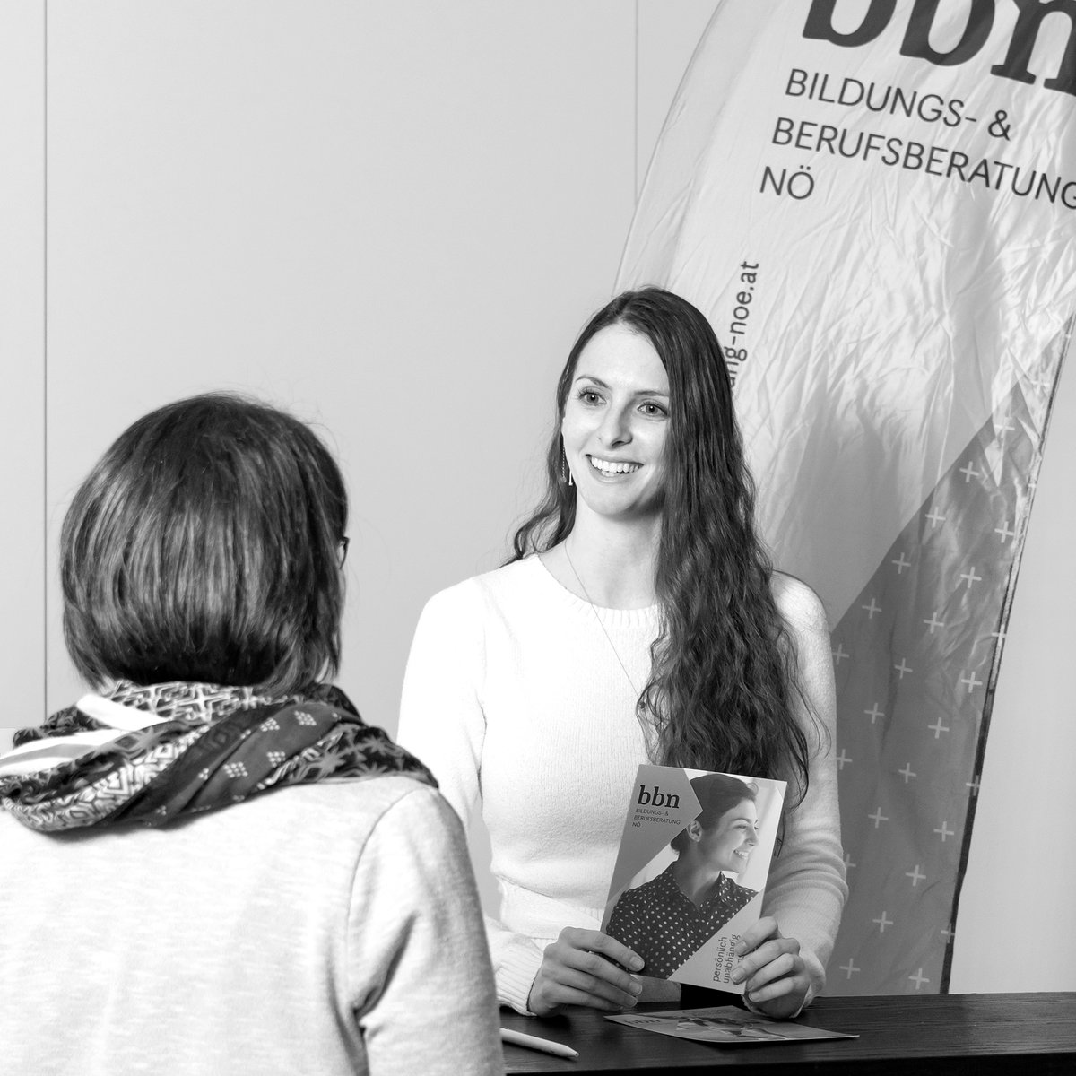 Eine Beraterin steht hinter dem Messestand der Bildungs- und Berufsberatung und eine Person steht davor.